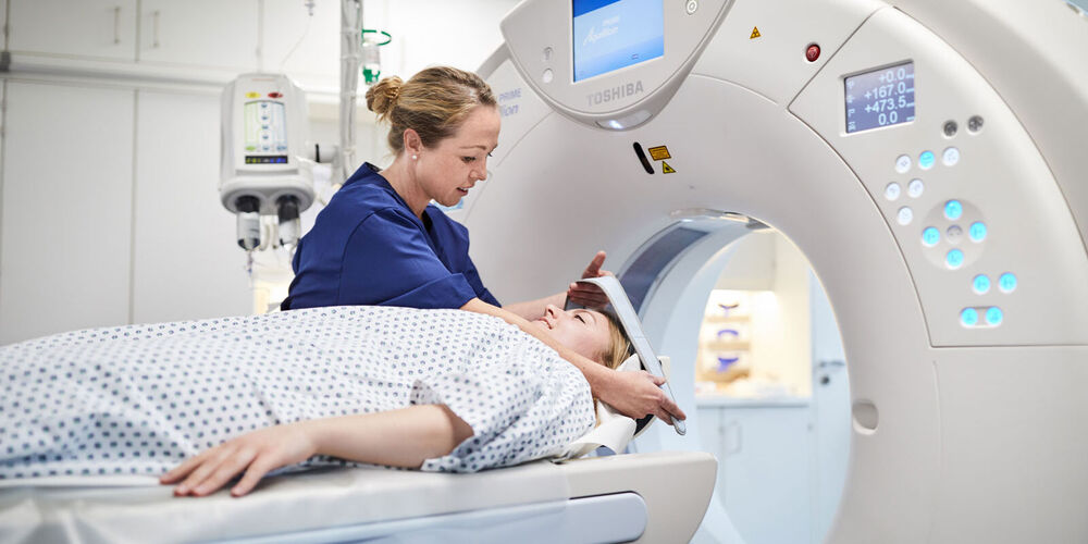 Eine junge Krankenpflegerin betreut eine Patienten, die in einer Röntgenröhre untersucht werden soll.