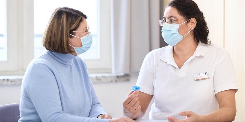 Eine Ärztin und eine Patientin sprechen miteinander. Beide tragen einen Mund-Nasen-Schutz.