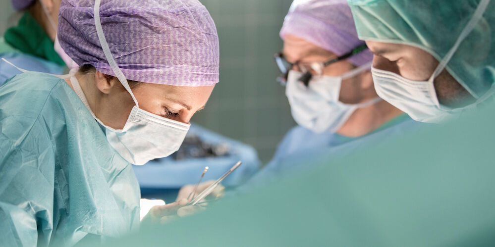 Operationssaal in dem einige Ärzte in Operationskleidung stehen und operieren.