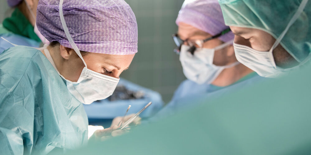 Operationssaal in dem einige Ärzte in Operationskleidung stehen und operieren.