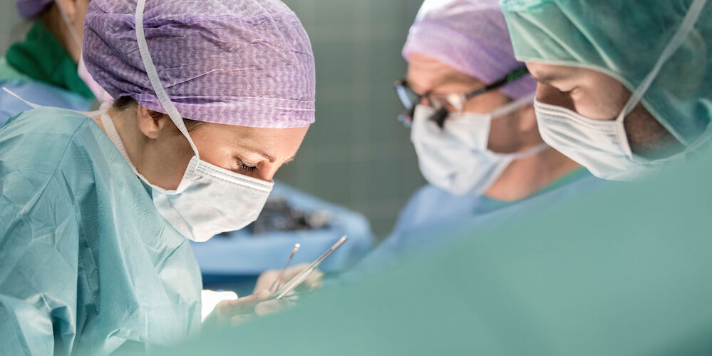 Operationssaal in dem einige Ärzte in Operationskleidung stehen und operieren.