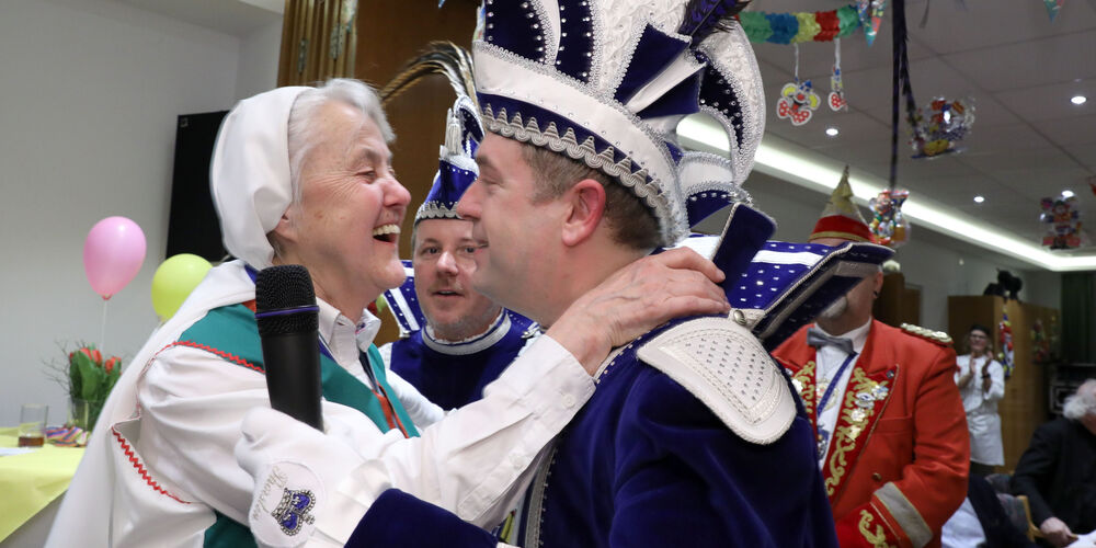 Einige Leute in Karnevalskostüm. Im Vordergrund umarmen sich eine Frau und ein Mann. 