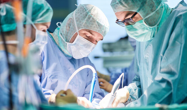 Operations in einem Operationssaal. Drei Ärzte in Operationskleidung stehen am Operationstisch und operieren.