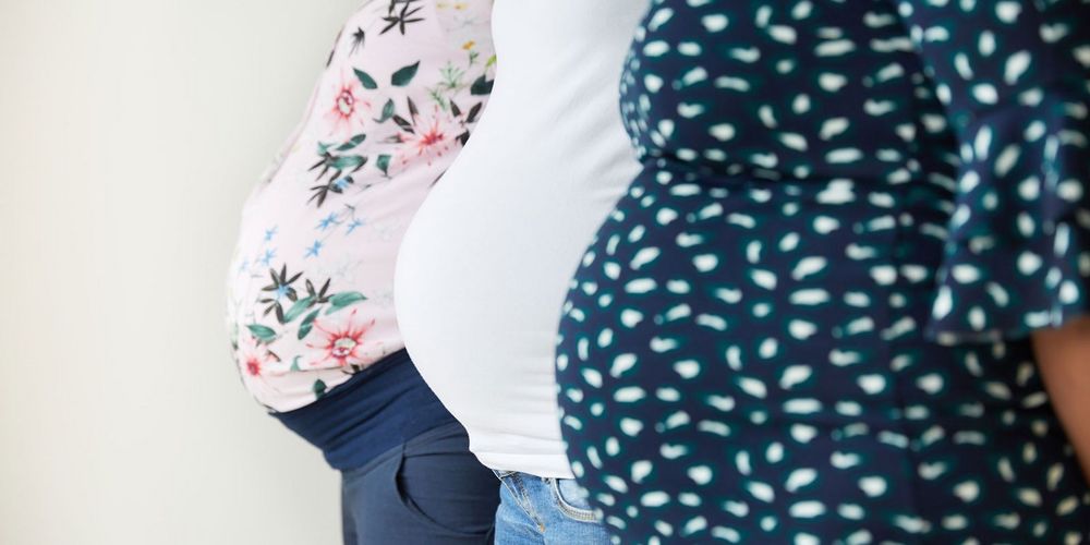 Drei schwangere Frauen zeigen hintereinander stehend ihren Babybauch in die Kamera
