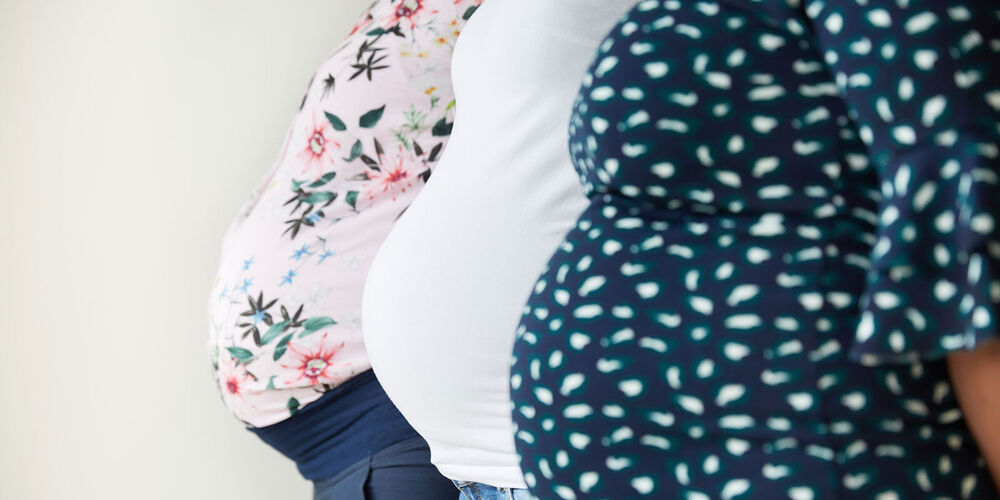 Drei schwangere Frauen zeigen hintereinander stehend ihren Babybauch in die Kamera