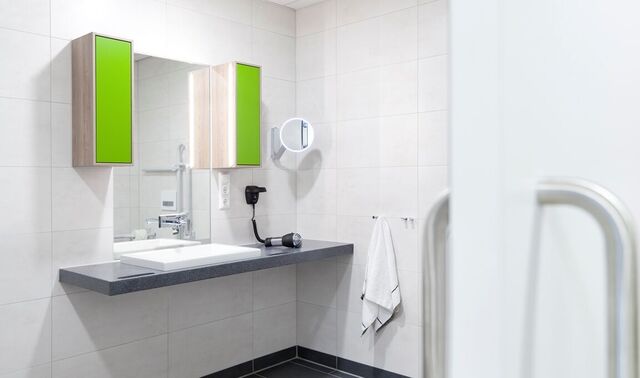 Modernes Badezimmer mit einem Waschbecken über welchem ein Spiegel mit zwei Schränken hängt. 