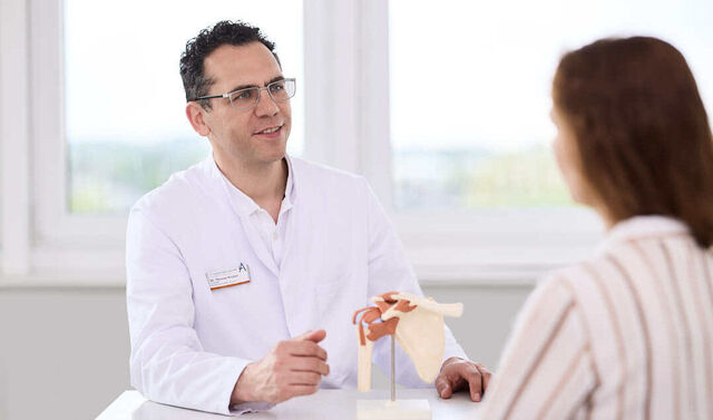 Ein Arzt erklärt einer Patientin anhand eines Hüftmodells ihre Erkrankung.