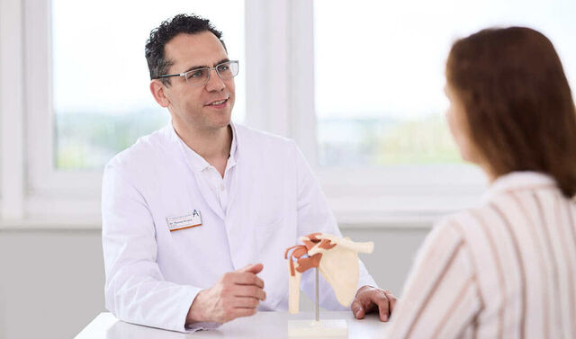 Ein Arzt erklärt einer Patientin anhand eines Hüftmodells ihre Erkrankung.
