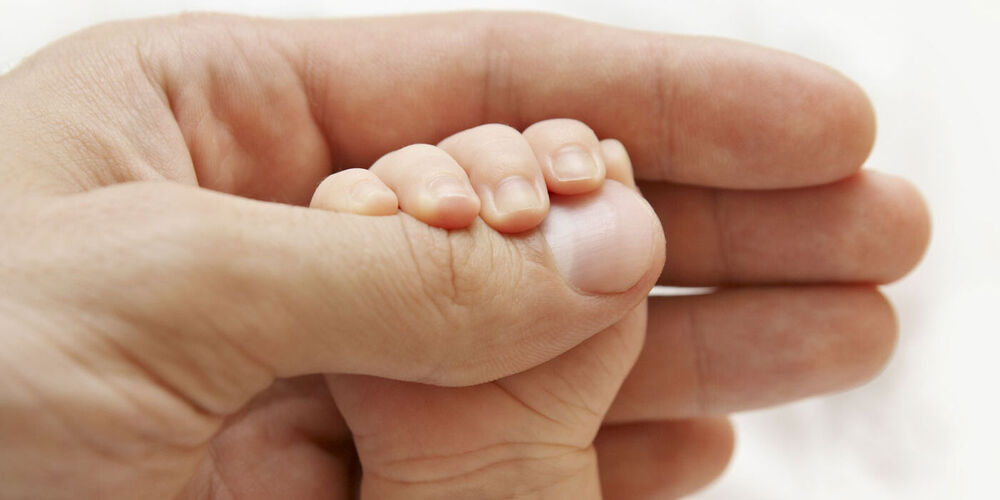 Die Babyhand umfasst den Daumen der Mutterhand.