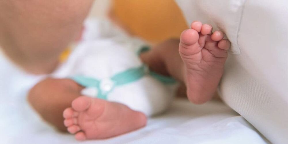Füße eines Neugeborenen von unten. Dieses liegt auf einer Decke.
