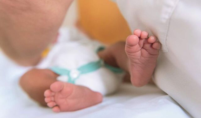 Füße eines Neugeborenen von unten. Dieses liegt auf einer Decke.