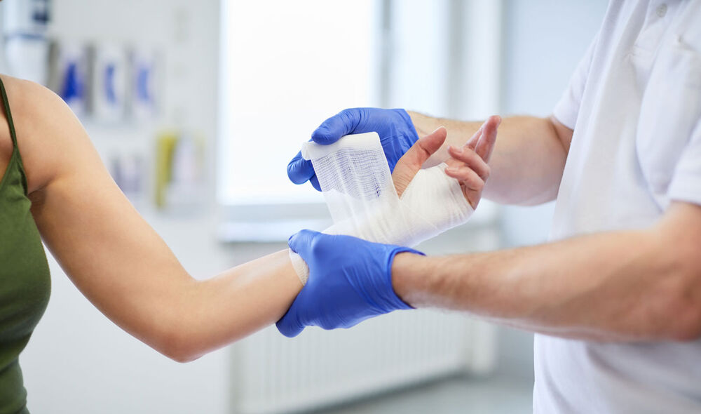 Mitarbeiter legt einer Patientin einen Verband um das Handgelenk. 