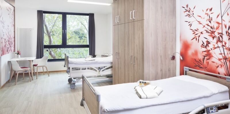 Patientenzimmer in der Klinik Neuwerk. In diesem stehen zwei Betten und ein Schrank, sowie ein Tisch mit zwei Stühlen.