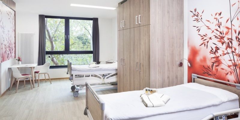 Patientenzimmer in der Klinik Neuwerk. In diesem stehen zwei Betten und ein Schrank, sowie ein Tisch mit zwei Stühlen.