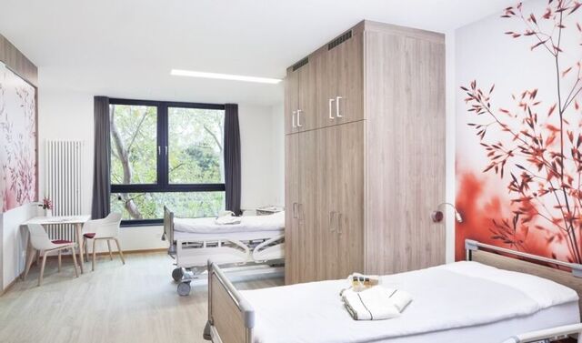 Patientenzimmer in der Klinik Neuwerk. In diesem stehen zwei Betten und ein Schrank, sowie ein Tisch mit zwei Stühlen.