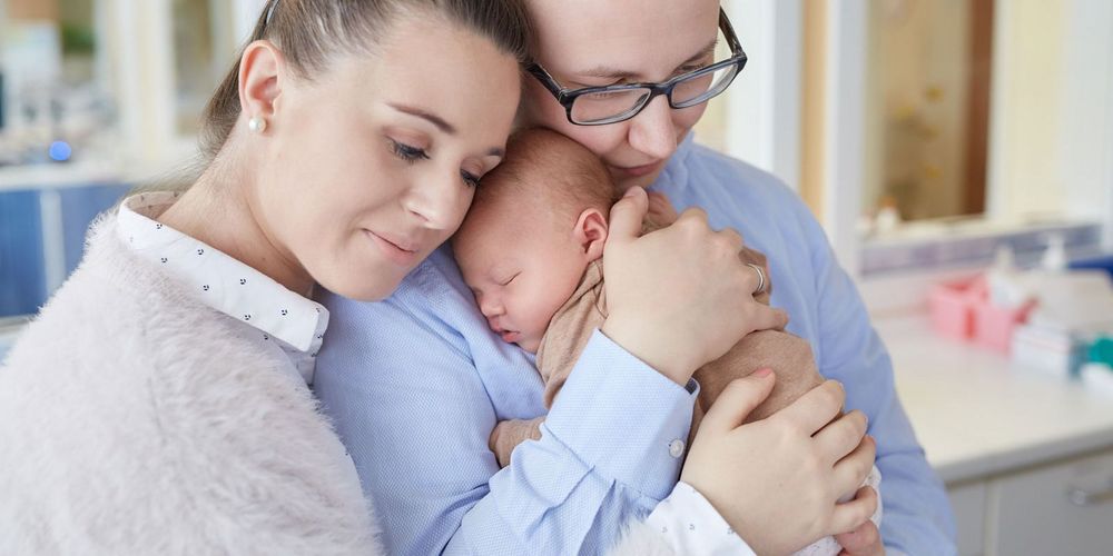 Ein junges Paar das sich umarmt und ihr neugeborenes Baby auf dem Arm hält.