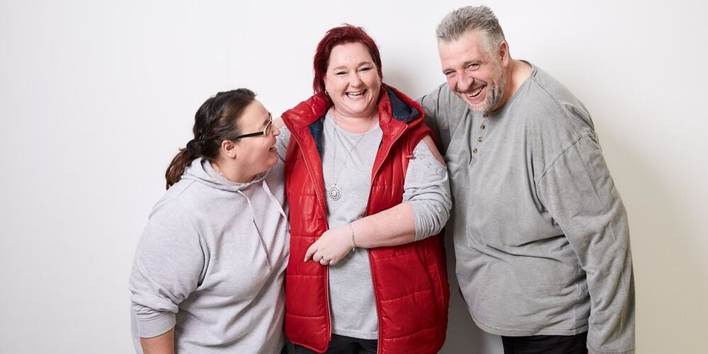Zwei Patientinnen und ein Patient stehen lachend vor einer Wand und albern miteinander.